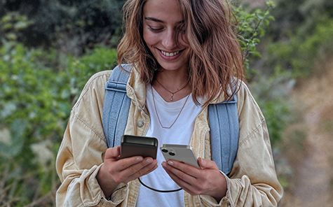 A woman is travelling in the mountains and charges her smartphone with a Hama Power Pack.
