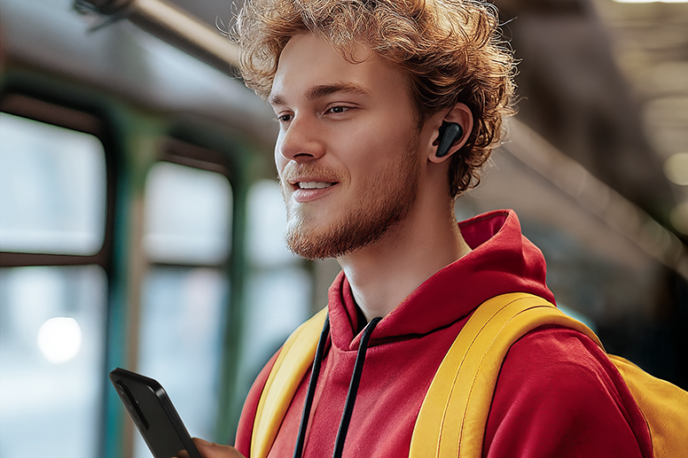Hombre con auriculares Bluetooth en los oídos y teléfono móvil en la mano en el tren.