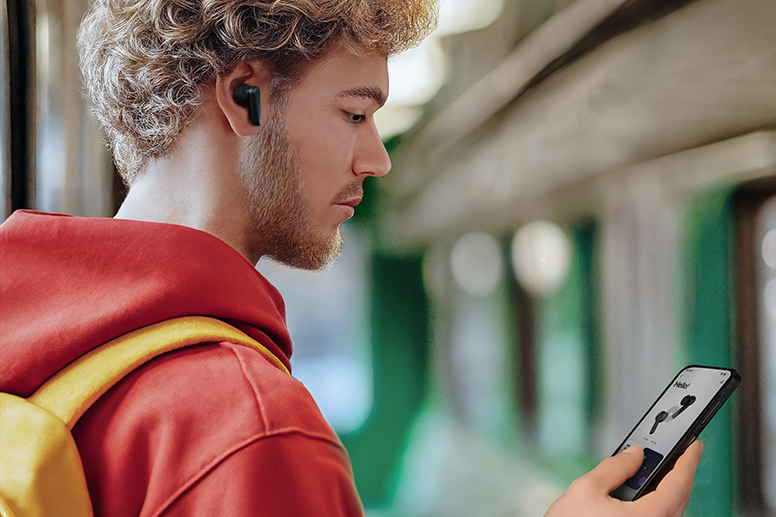 Hombre sosteniendo un teléfono móvil. La aplicación Hama para controlar los auriculares Bluetooth está abierta en la pantalla.