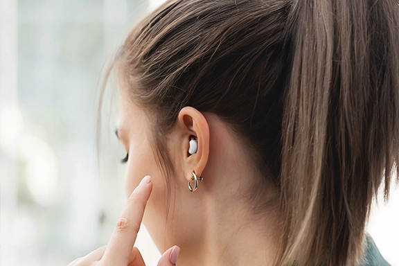Mujer con auriculares Spirit Calm en los oídos levanta el dedo hacia la oreja para controlar la música.