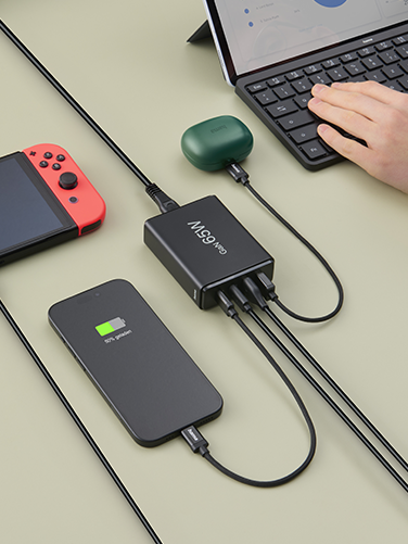 Sobre una mesa hay un portátil abierto, un smartphone, una Nintendo Switch y unos auriculares Bluetooth. Todos se cargan simultáneamente a través de la estación de carga Hama.