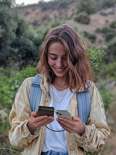 Una joven hace senderismo por el campo y utiliza su smartphone mientras lo carga con el Hama Power Pack «PD 20»