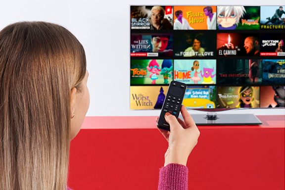 Una mujer maneja varios servicios de streaming desde el sofá con un mando a distancia